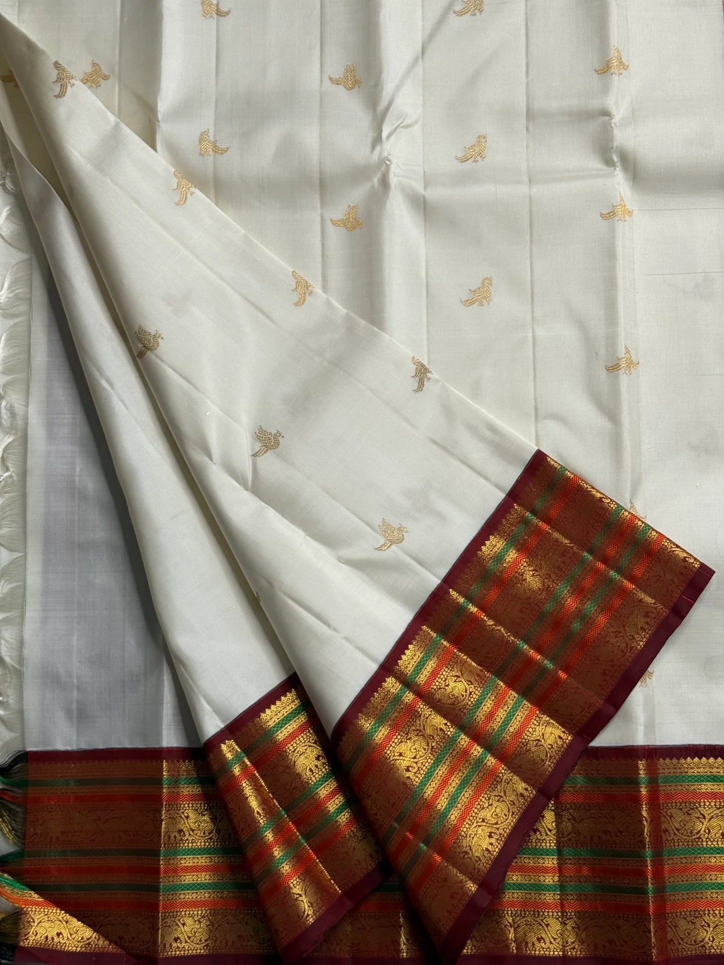 Parakkum Kili — Ivory Pure Silk Kanchipuram
Ivory body with fine zari coin buttas ✨
Rust-orange korvai borders with mayil & temple motifs 🌸
Grand rust-orange zari brocade pallu with tassels 🪔
Silk Mark Certified • Free Shipping USA • Ships in Two Weeks