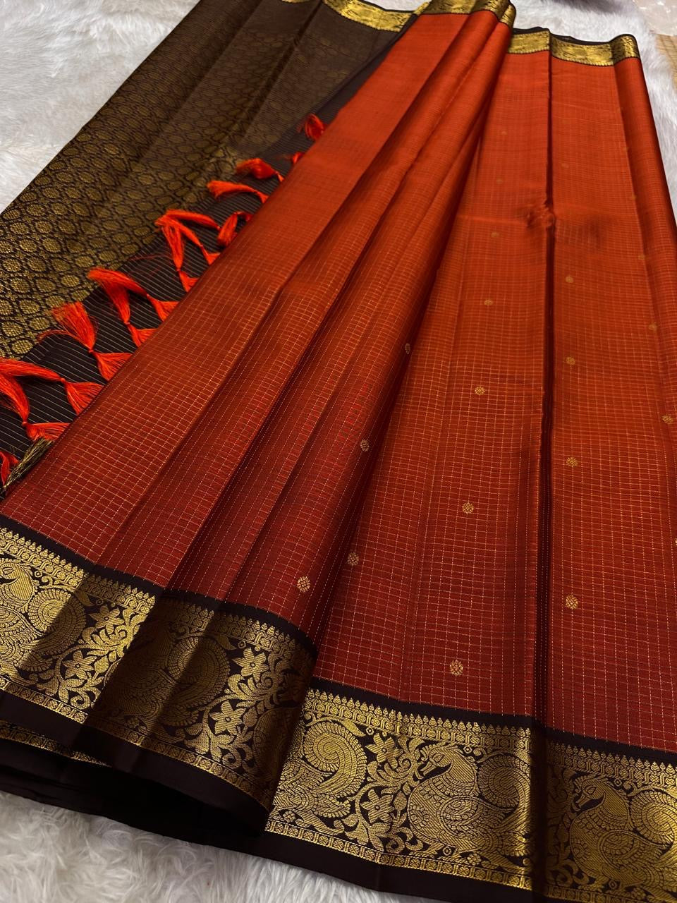 Mantra – Rust brown with coffee brown Kanchipuram Silk Saree with zari Checks with small buttas all over and Antique Peacock zari Border showcasing regal peacocks and floral vines. A richly detailed pallu completes this heritage Zari kattam