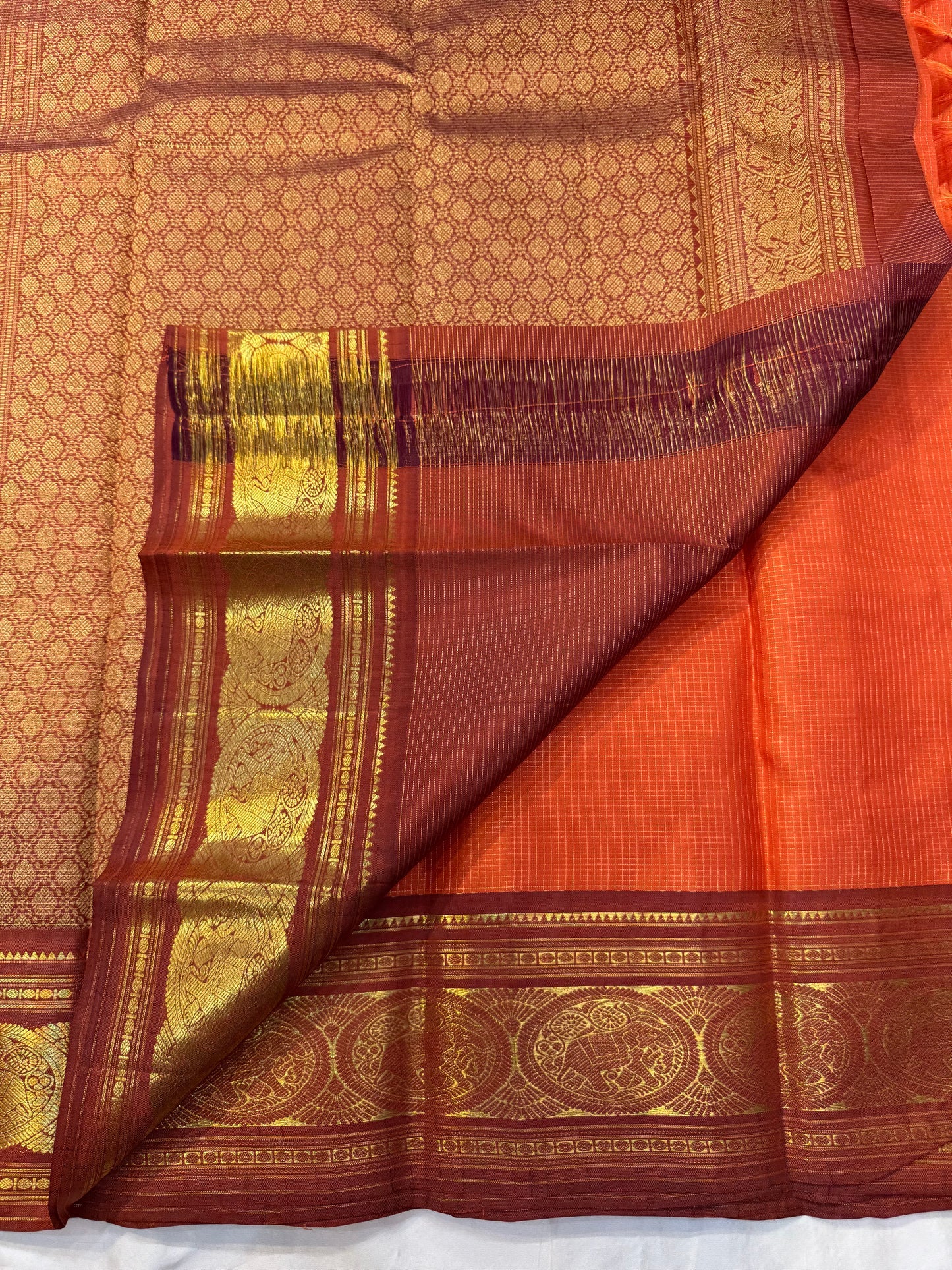 TEJAS – Vibrant Rust Orange Podi Kattam Kanchipuram Silk Saree
Micro-checks body with scattered gold chakram buttas; rich contrast maroon korvai borders
Grand circular annapakshi medallions in lustrous zari; ornate-jaal pallu & tassels
Silk Mark