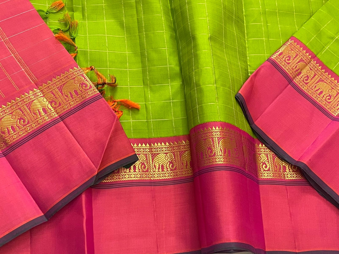 Valli Pachai – Kanchipuram Pure Silk Saree
Parrot-green body in kattam (grid) checks with subtle zari lines
Korvai contrast rani-pink borders featuring gaja (elephant) procession & temple reku motifs
Rich rani-pink zari pallu with vertical bands