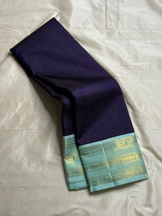Moonlit & Mint Checks – Korvai Kanchipuram Silk Saree
Pure handloom silk | Deep indigo body in micro checks (podi kattam)
Mint-green korvai border with gold muthuseer coin bands & vines
Rich mint-green zari-pallu |
Silk mark certified ships in 2 weeks
