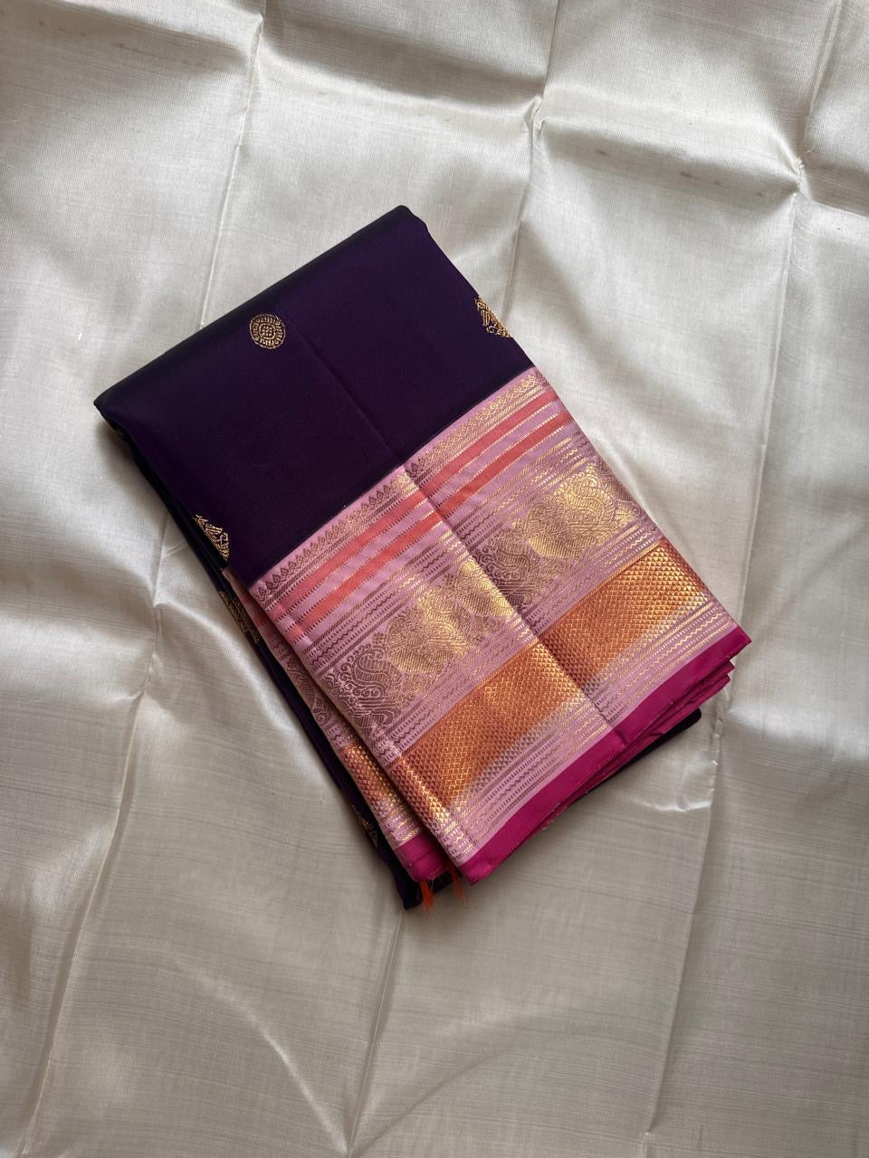 Shyamala—named after the deep, dark shade it embodies 💜 A pure Kanchipuram silk masterpiece with a rich purple body sprinkled with golden zari buttas. The contrast pink border glows with floral and paisley zari motifs, accented in coral and rose-gold, wh
