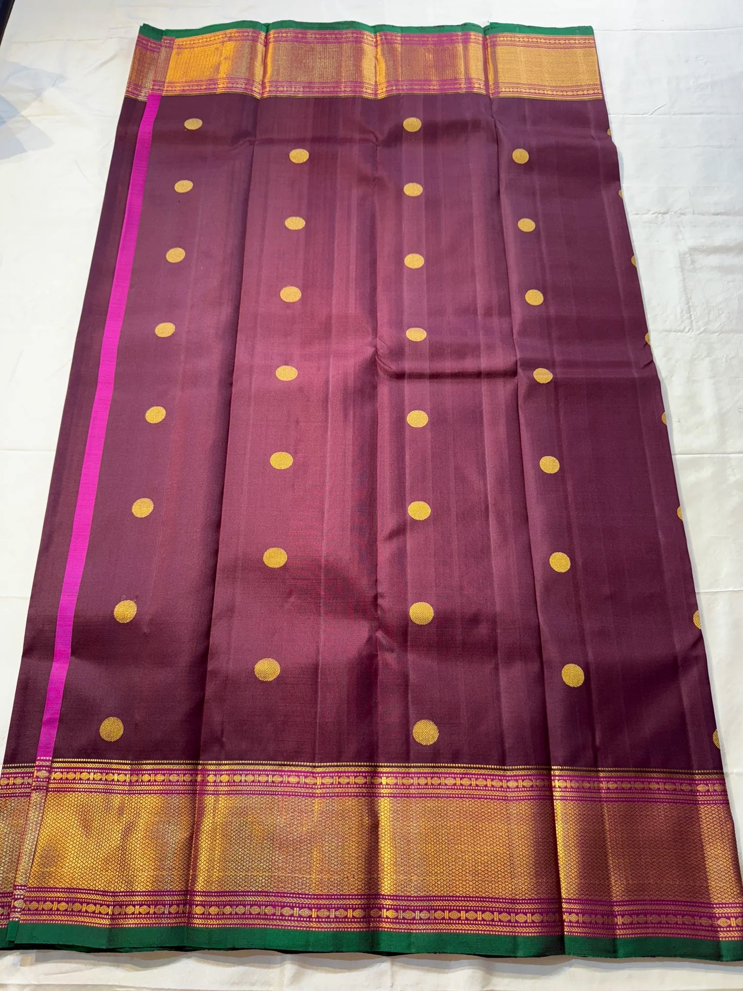 Plum & Magenta Round Butta – Pure Kanchipuram Silk Saree
Deep plum body with bold round gold zari buttas
Contrast green selvedge & gold tissue borders with magenta detailing
Grand magenta-pink pallu with full zari diamond jaal & geometric panels
Silk Mark