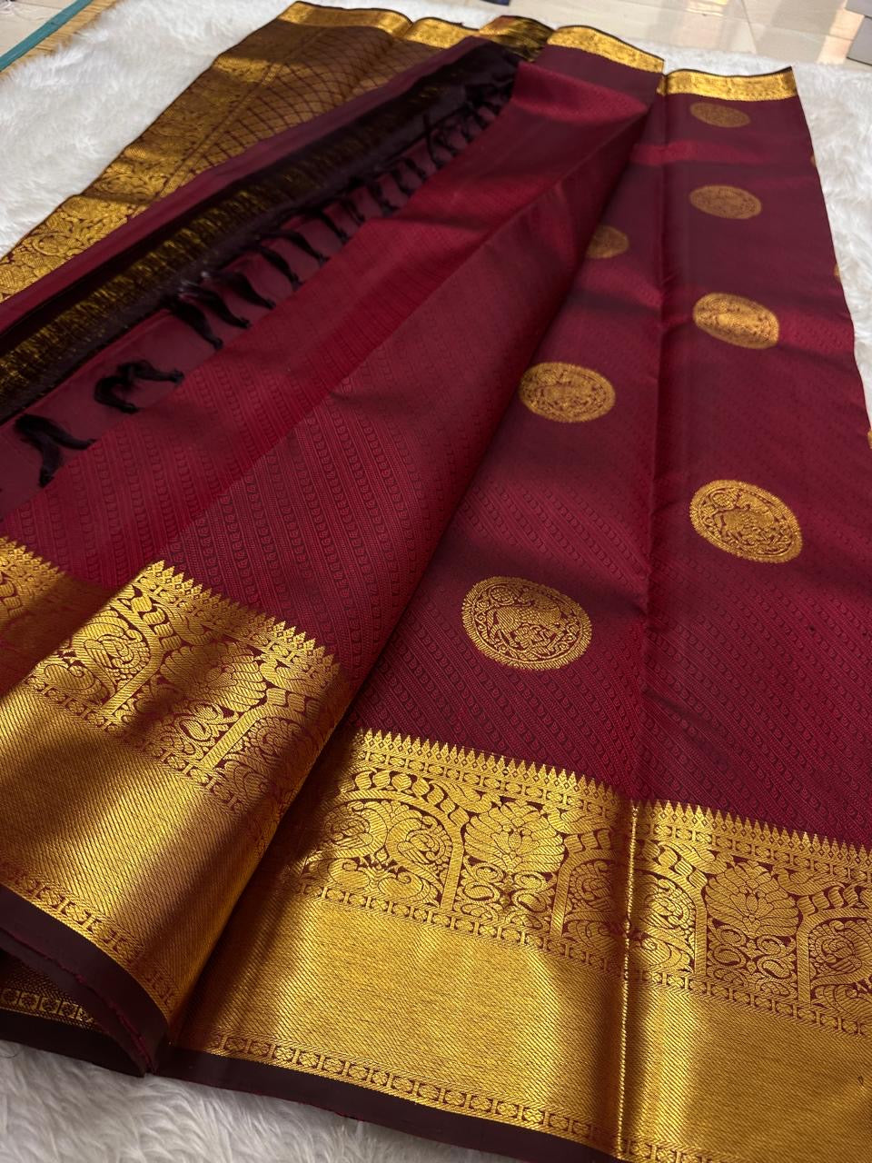 A majestic maroon Kanchipuram silk saree, adorned with intricate golden zari featuring the mythicalYazhi (Yali ) motifs—a symbol of divine strength and protection in Hindu mythology. The grand temple-style gold border adds depth and regality, making this