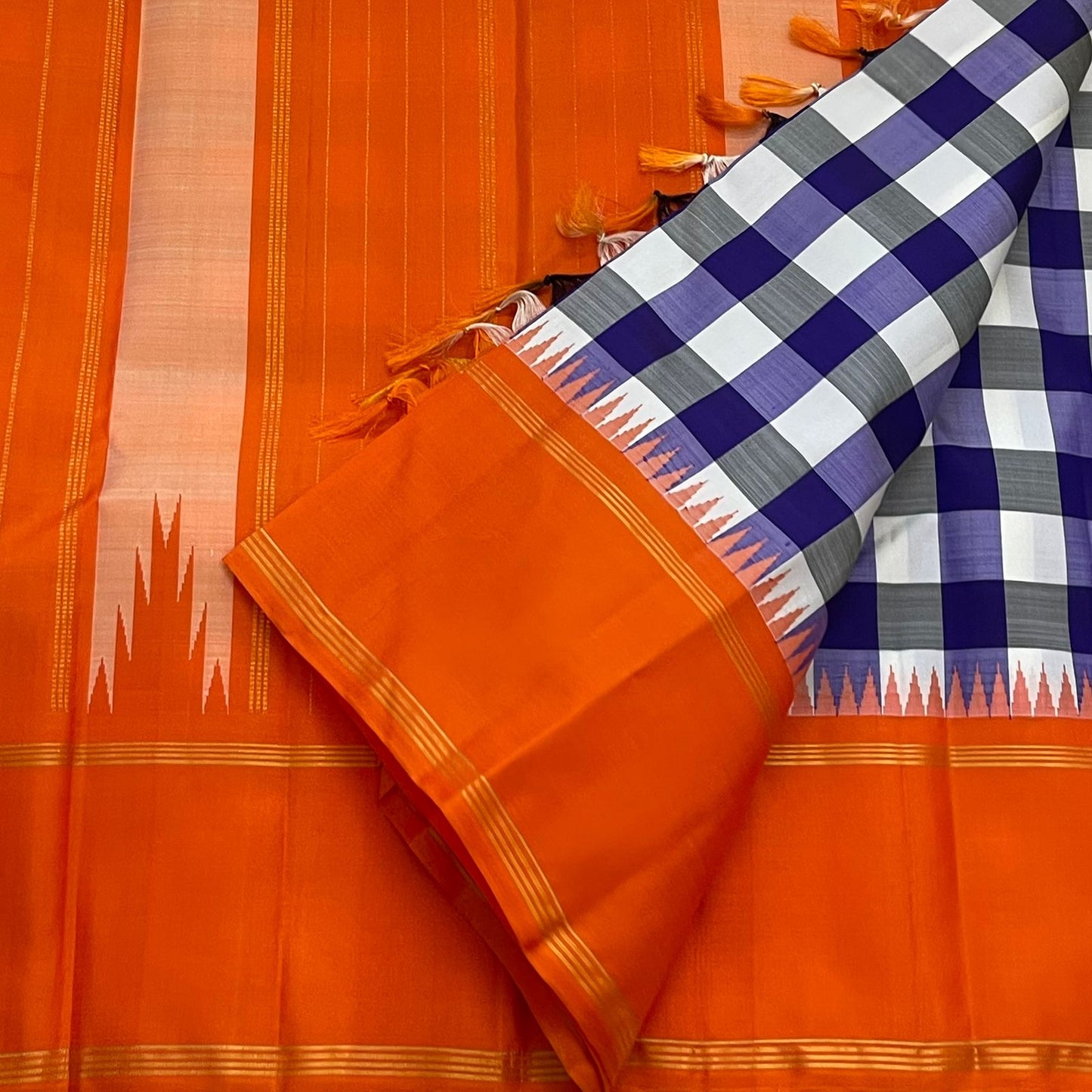 Indigo–Tangerine Checkmate — Pure Silk Kanchipuram
Bold indigo–lilac–white buffalo checks with ash accents ✨
Vibrant tangerine korvai border with temple (reku) teeth 🌸
Solid tangerine pallu with fine thread stripes & tassels 🪔
Silk Mark Certified •