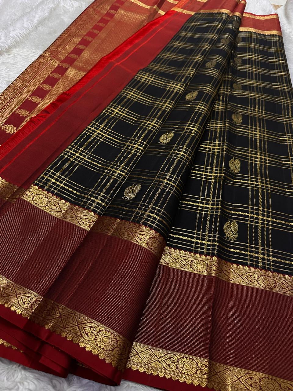 Kanmani Karuppu Kattam Ruby – Pure Kanchipuram Silk Saree
Deep black body with gold kattam checks & peacock buttas
Contrast ruby-red korvai borders
Grand ruby-red pallu with floral & lattice zari motifs
Silk Mark Certified | ships in 2 weeks