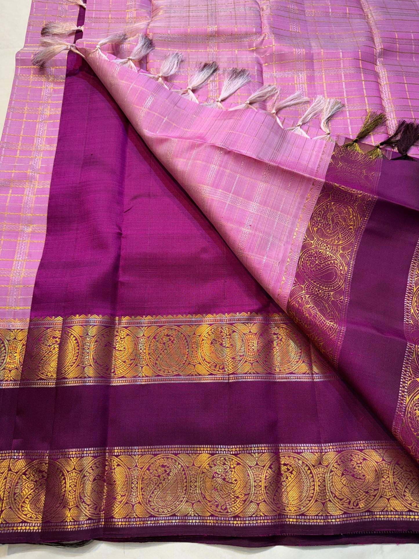 Mauve Mayil Mukham — Kanchipuram Pure Silk
Pastel-mauve pink  body with delicate zari wide kattam checks
Deep plum korvai border with grand mayil (peacock) chakram motifs
Copper-rose chevron zari pallu & plum contrast blouse
Silk Mark Certified • Free
