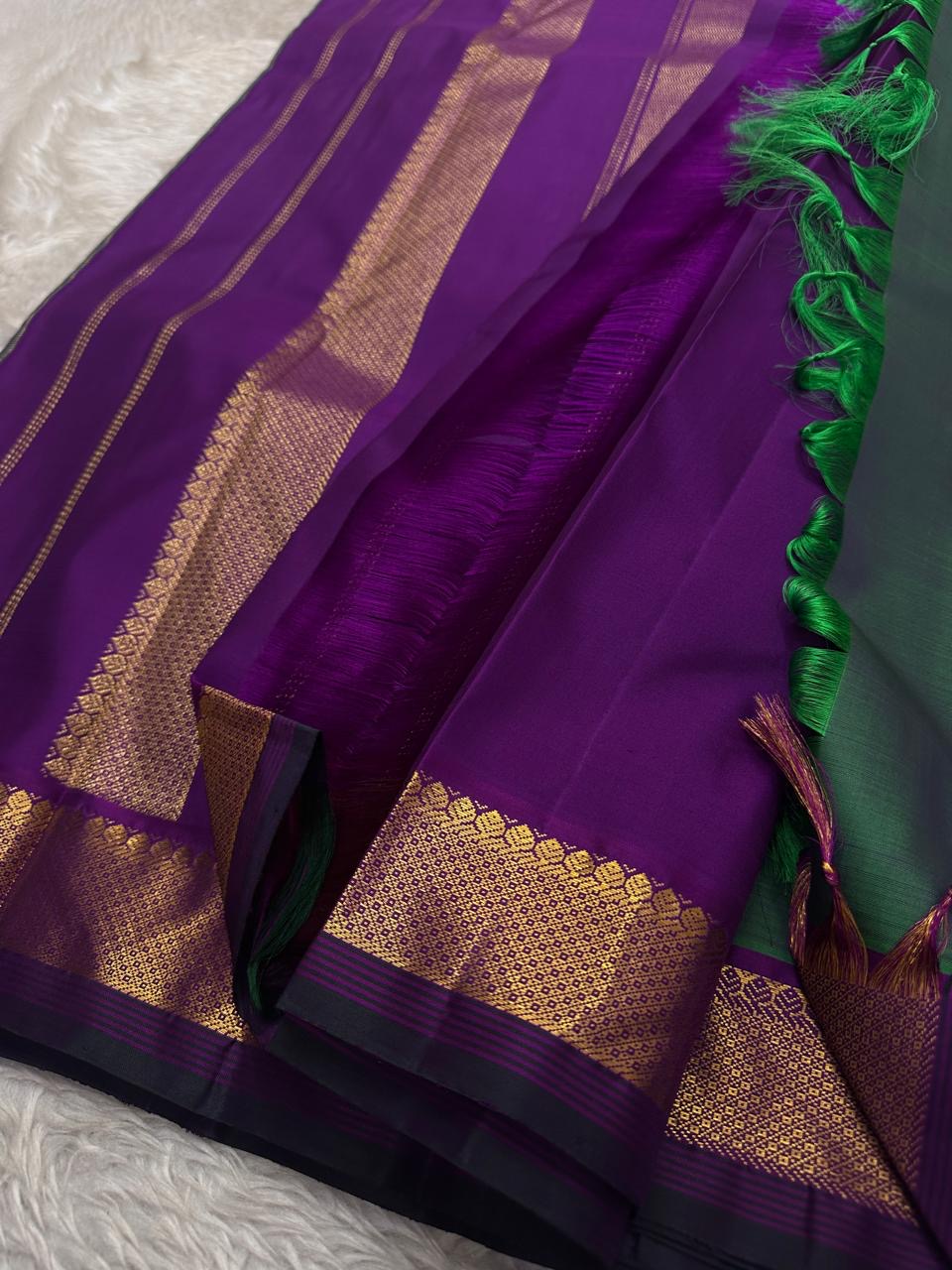 Varnam is a pure Kanchipuram silk saree in rich emerald green with subtle dual-tone shading. Woven gold zari buttas dot the body, while a petite purple border woven with intricate zari adds refined contrast. Arai maadam Pallu, jewel toned classic !