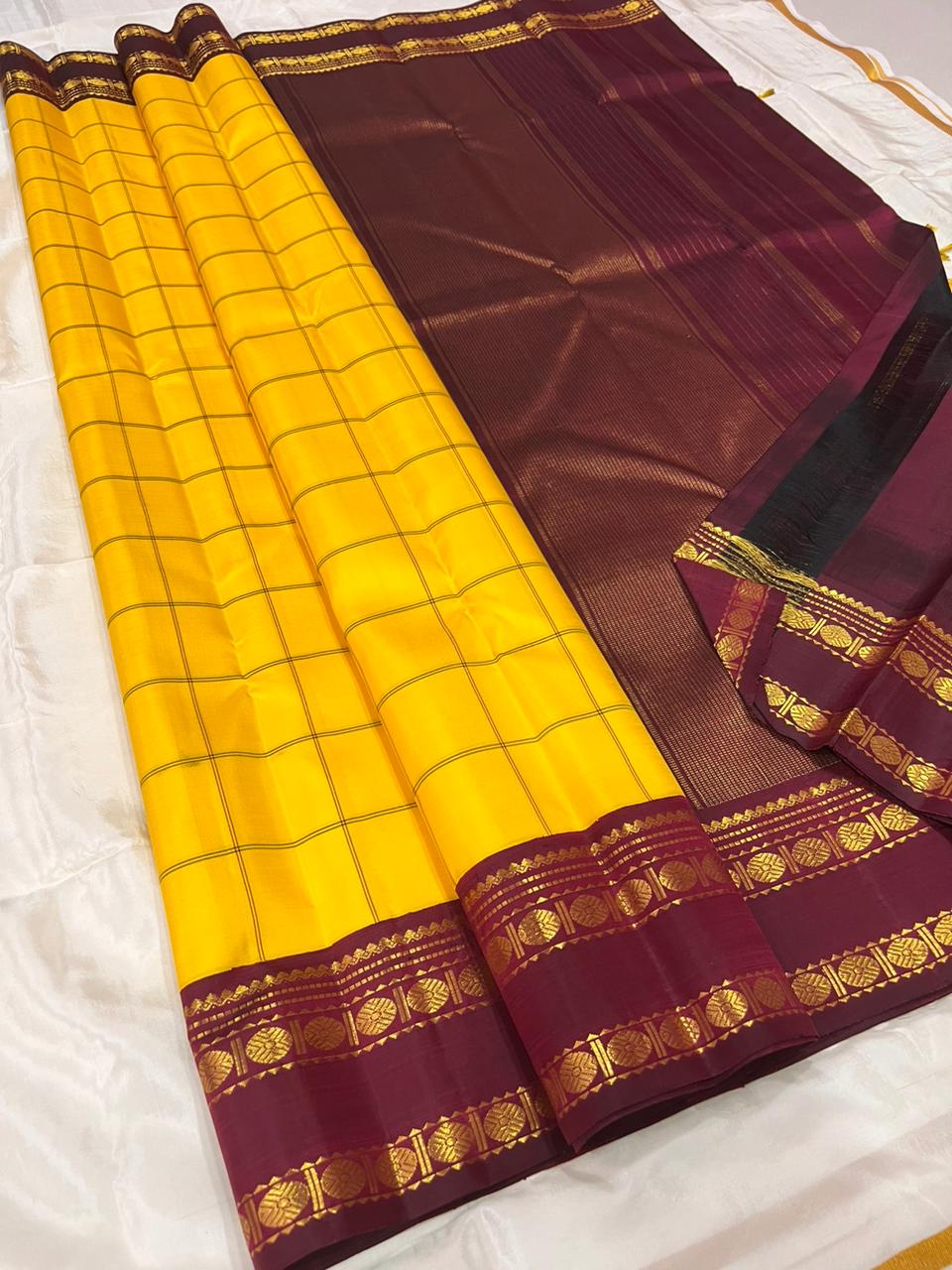 Marigold Yellow & Arakku Pure Silk Kanchipuram Saree
Classic kattam checks across the radiant marigold body
Deep arakku-maroon korvai borders with coin medallion zari
Rich maroon pallu with traditional zari  motifs
Silk Mark Cert • Ships in 2 weeks