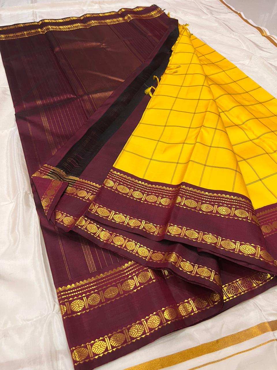 Marigold Yellow & Arakku Pure Silk Kanchipuram Saree
Classic kattam checks across the radiant marigold body
Deep arakku-maroon korvai borders with coin medallion zari
Rich maroon pallu with traditional zari  motifs
Silk Mark Cert • Ships in 2 weeks