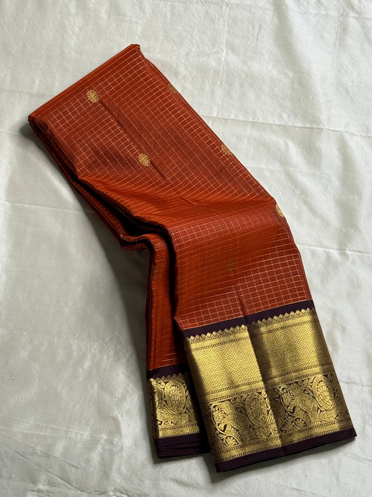 Rust Orange Kattam & Purple Korvai – Pure Kanchipuram Silk Saree
Rust-orange checks with delicate gold buttas and contrast purple korvai borders
Grand purple zari-pallu | Contrast purple blouse | Fall & Pico Done
Silk mark certified ships
