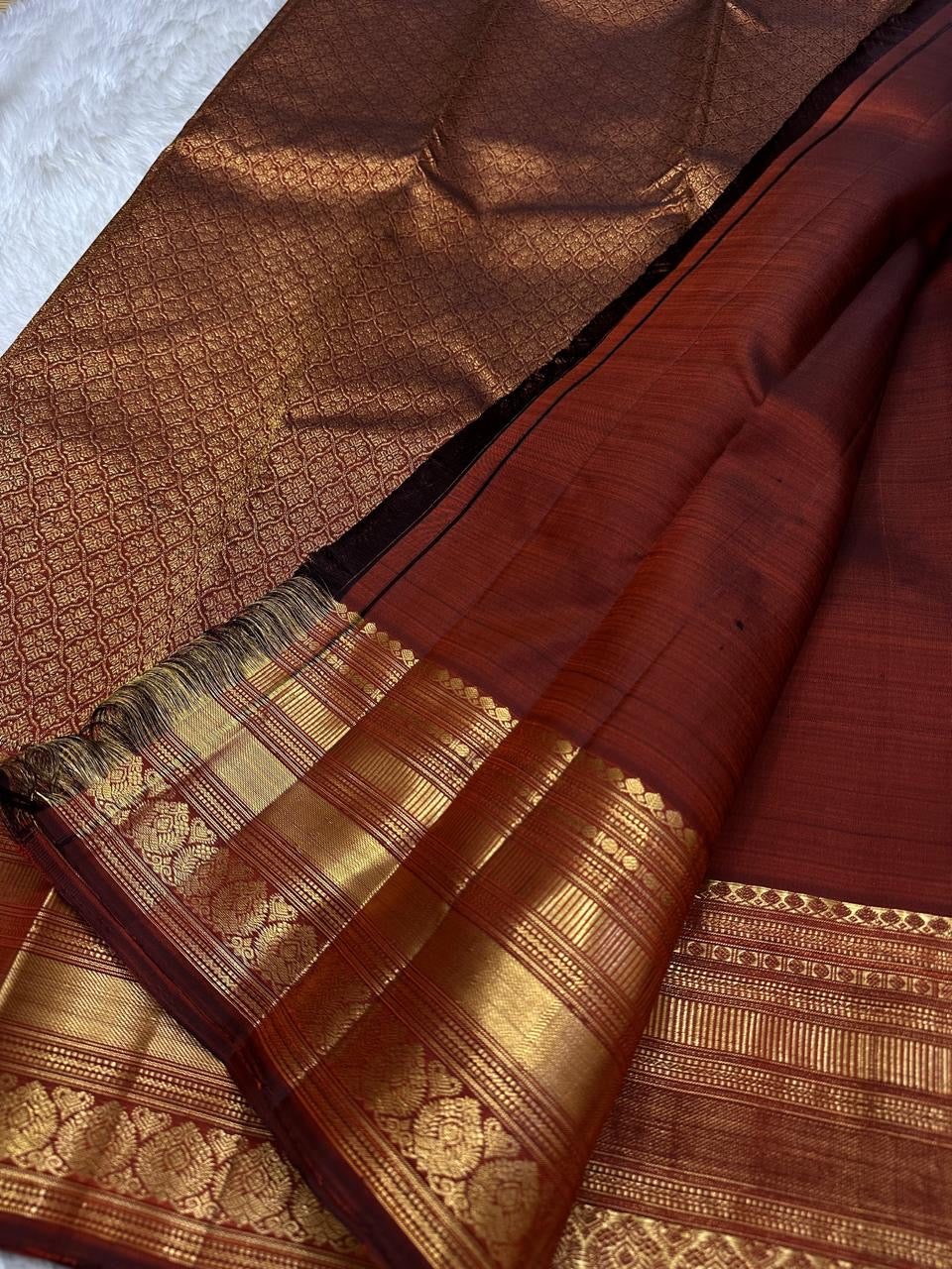 Gilded Rust – Pure Kanchipuram Silk Saree
Deep rust body with delicate paisley zari buttas 🌿
Antique-gold border featuring kaddi stripes & floral motifs ✨
Grand brocade pallu with lattice jaal & floral vines 🕊️
Silk Mark Certified, delivery in 2 weeks