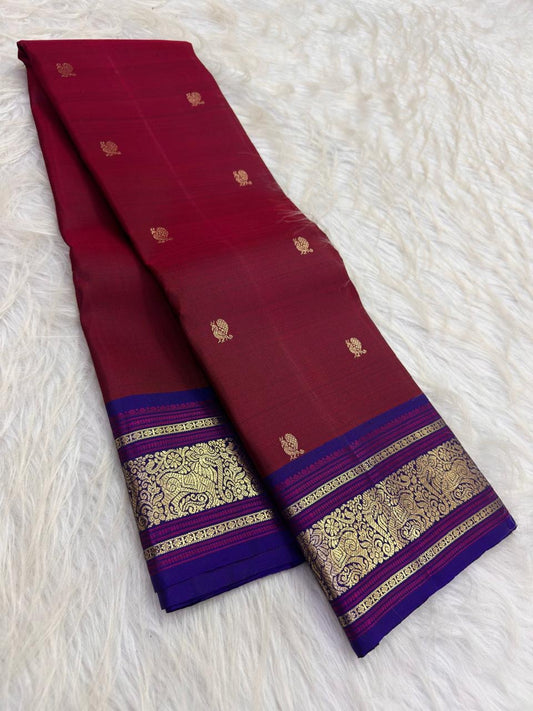 Close view of small gold peacock buttas scattered over an arakku-red body and deep royal violet-indigo border with framed panels of curling gold peacock and floral motifs and parallel fine zari stripes on pure silk Kanchipuram saree