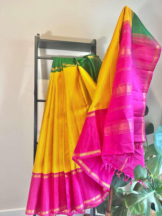Swarna Kattam Ganga Jamuna — Pure Silk Kanchipuram Saree
Golden mustard kattam checks body • Dual korvai borders in rani pink & emerald green
Rich zari pallu with radiant festive sheen
Contrast emerald blouse with zari selai finish
Silk Mark Certified •