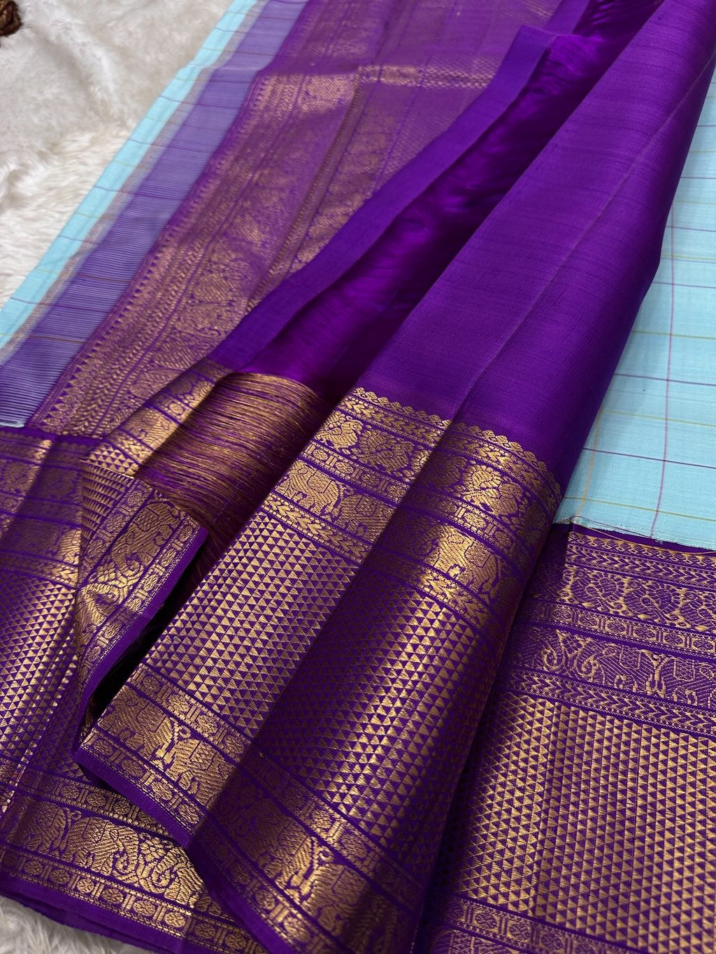 Aqua Amethyst zari kattam Pure Kanchipuram Silk Saree with blue Checks & Purple Border
Radiant sky-blue silk woven with delicate golden checks.
Grand purple korvai borders with elephant and floral motifs.
Silk Mark Certified, delivery in 2 weeks