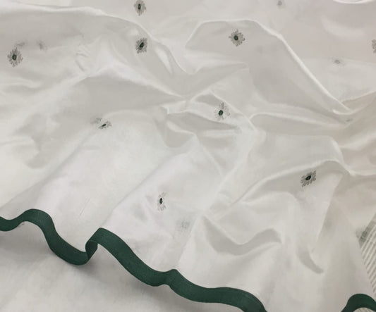 Draped in ivery white , this pure silk Chanderi saree glows with a gentle sheen and graceful vertical zari lines. Delicate diamond meenakari motifs and finely woven borders lend a touch of tradition, while the contrast green selvedge adds a subtle edging