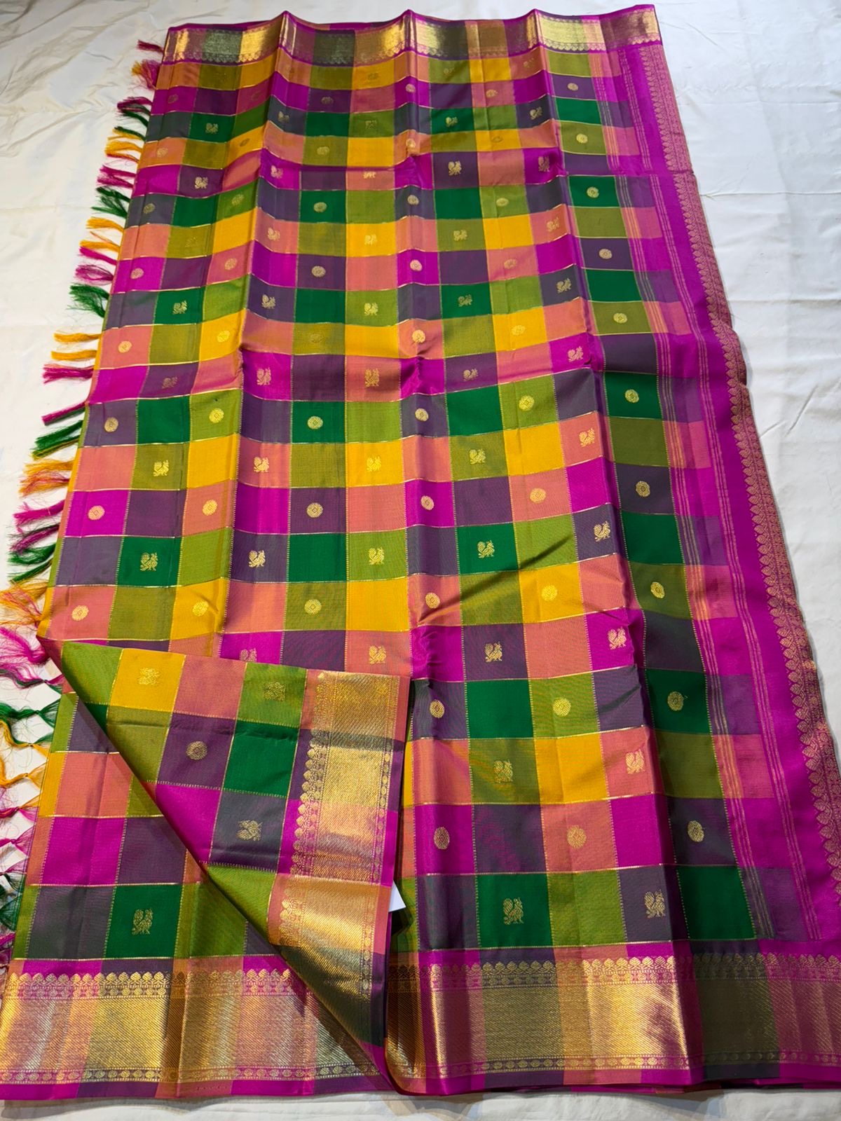 Pallavi – Kanchipuram Paalum pazhamum checks/ Zari kattam Silk Saree in Turmeric, Mango, Leaf Green & Beetroot Pink Checks.
Finished with a vibrant magenta border and rich gold zari pallu.