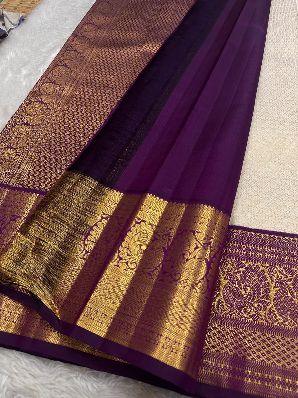 Ivory silk meets tradition in this elegant Kanchipuram saree. With a deep purple border and Mayuri motifs, it’s perfect for moments that call for quiet richness.