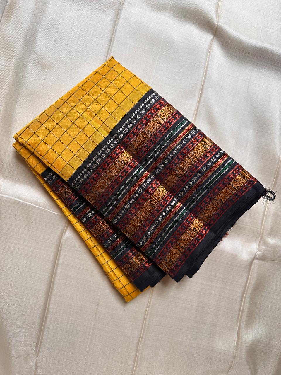 Marigold Mani Kattam – Pure Kanchipuram Silk Saree
Vibrant marigold yellow body with classic kattam checks
black borders with elephant & floral zari motifs
Rich black pallu adorned with green & zari stripes . Silk Mark Certified, delivery in 2 weeks