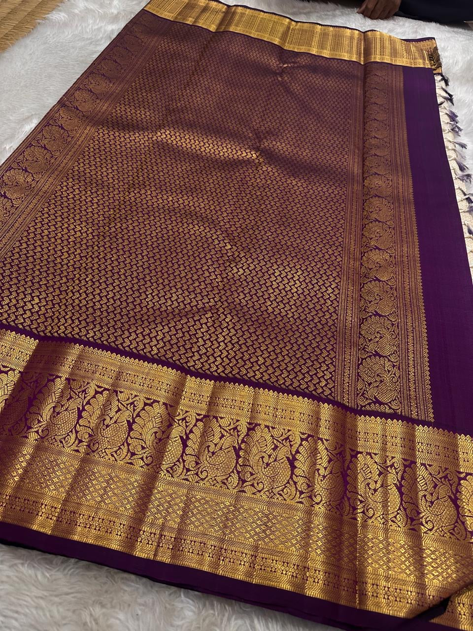 Ivory silk meets tradition in this elegant Kanchipuram saree. With a deep purple border and Mayuri motifs, it’s perfect for moments that call for quiet richness.