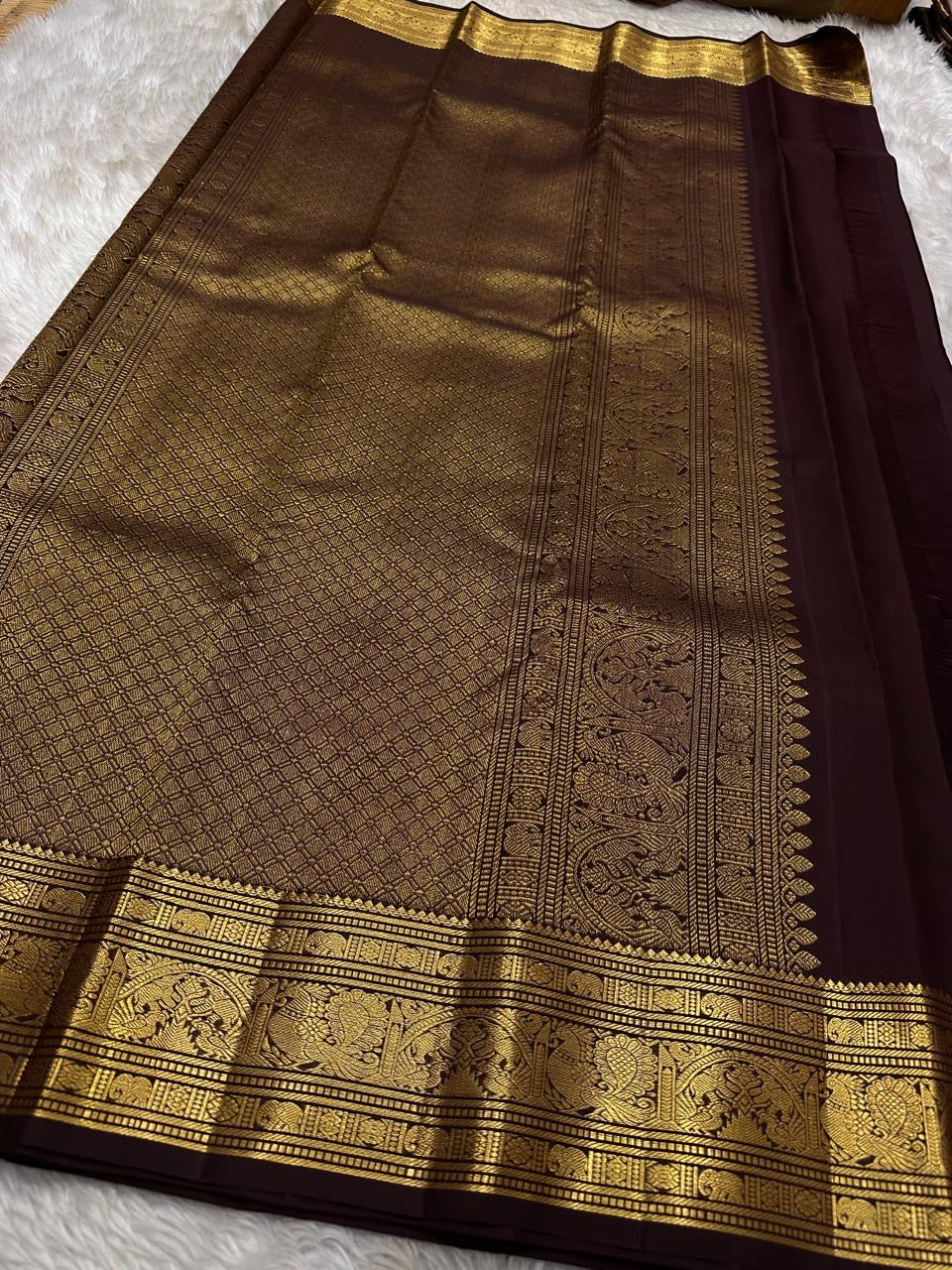 Kavi — oosi kattam Pure Kanchipuram Silk Saree
Burnt Orange (saffron–rust) body
Deep coffee-maroon contrast border with grand antique-gold zari
Rich brocade pallu; peacock & floral vines in the border
Silk Mark Certified