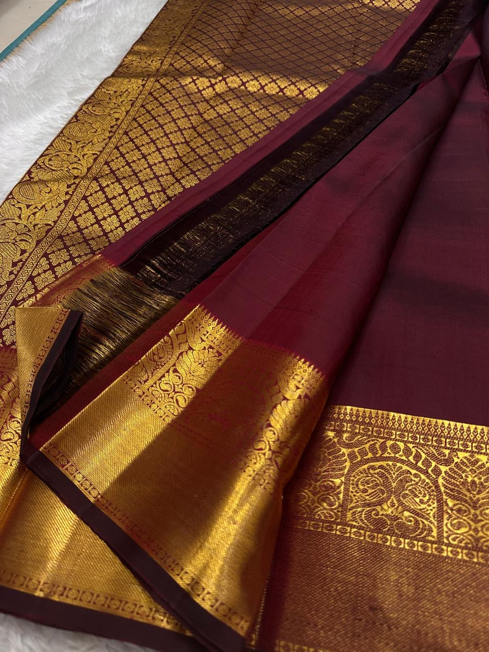 A majestic maroon Kanchipuram silk saree, adorned with intricate golden zari featuring the mythicalYazhi (Yali ) motifs—a symbol of divine strength and protection in Hindu mythology. The grand temple-style gold border adds depth and regality, making this