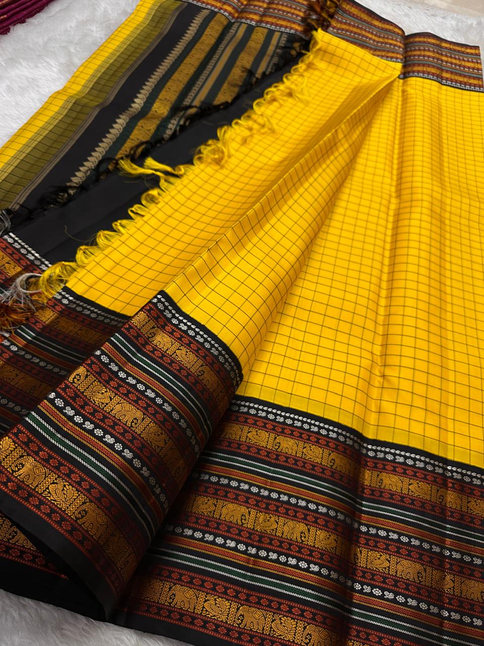 Marigold Mani Kattam – Pure Kanchipuram Silk Saree
Vibrant marigold yellow body with classic kattam checks
black borders with elephant & floral zari motifs
Rich black pallu adorned with green & zari stripes . Silk Mark Certified, delivery in 2 weeks