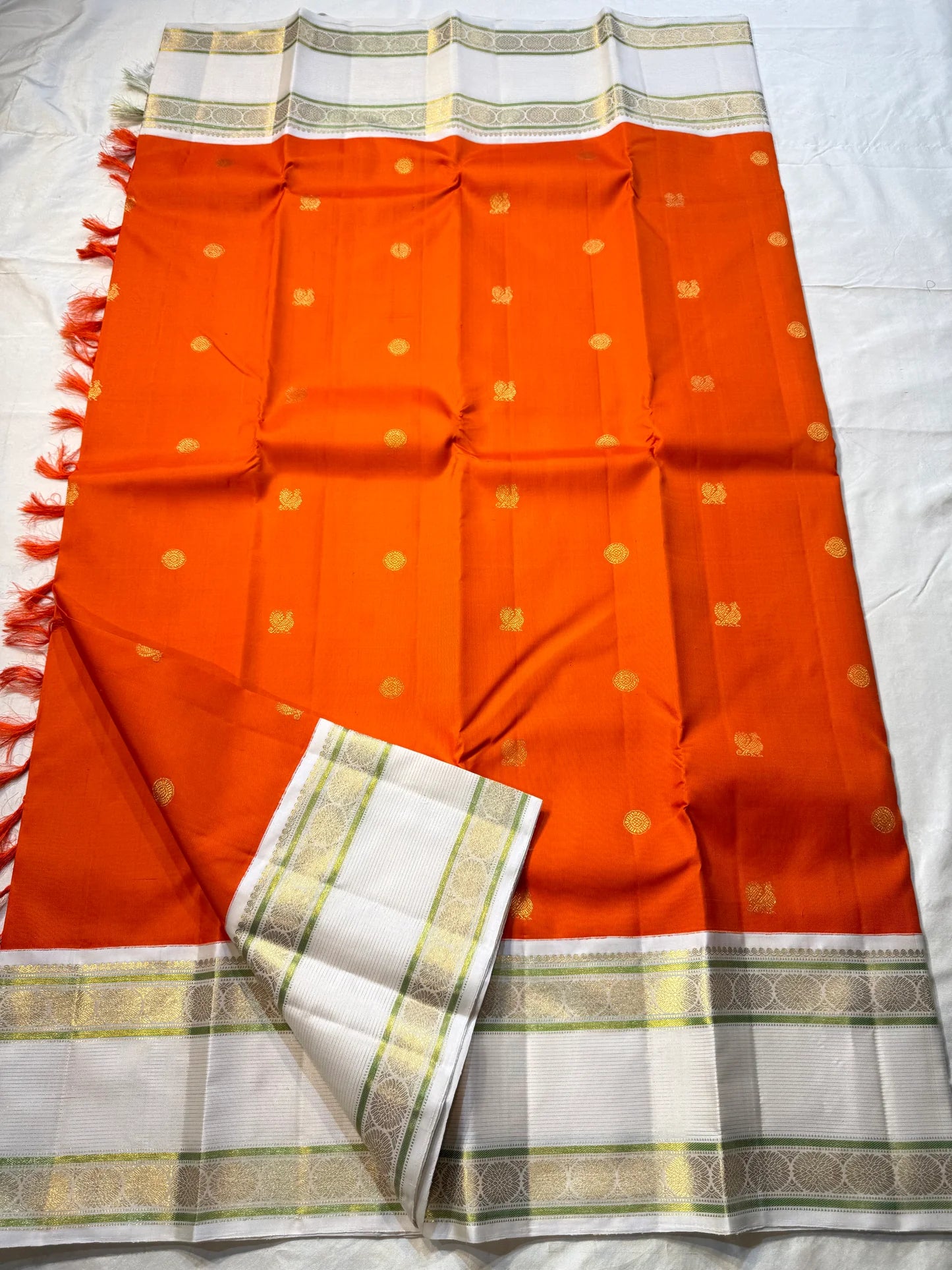 Kesar Chakram – Pure Kanchipuram Silk Saree
Rich Kesar Orange Body with Golden Chakram Buttas
Ivory Korvai Borders with Zari Rosette Motifs & Green Selvedge
Grand Ivory-Gold Brocade Pallu with Orange Tassels
Silk Mark Certified | ships in 2 weeks