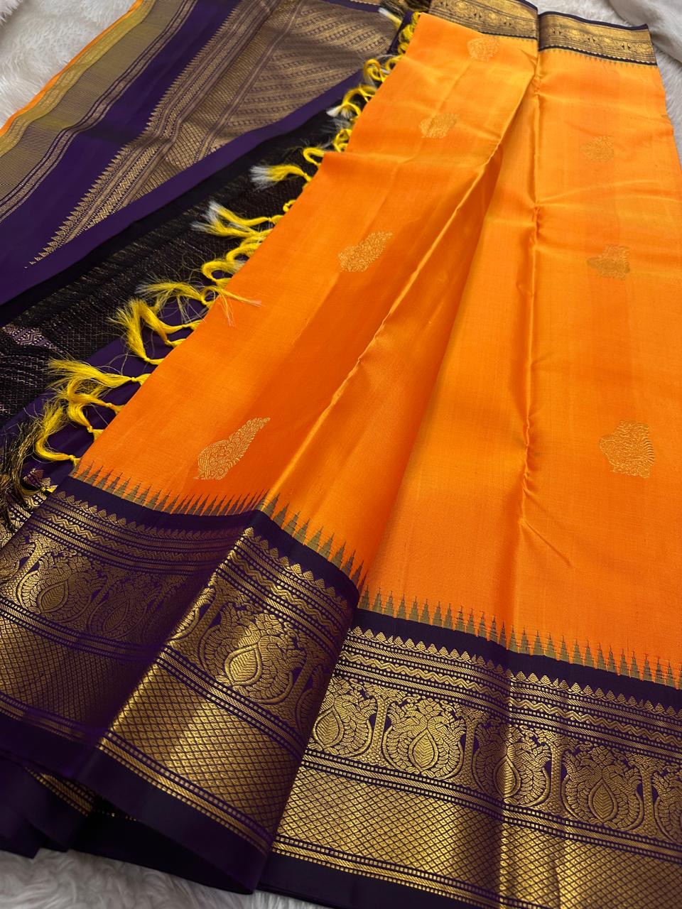 Pure Kanchipuram Silk Saree – Saffron-Orange Body with Gold Zari Paisley Buttas
Contrast Deep Purple Korvai Borders with Intricate Temple & Floral Motifs
Grand Purple Zari Pallu with Diagonal zariWeave . Silk mark , ships in 2 weeks