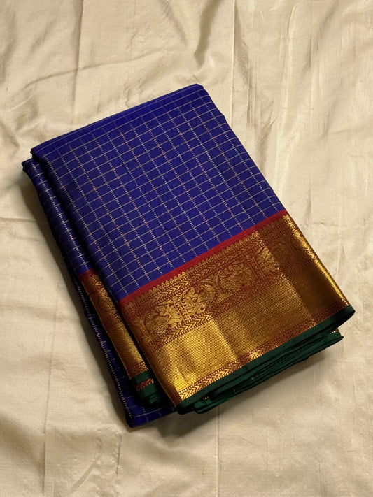 Neela Ratnam — Pure Silk Kanchipuram
• Cobalt-blue kattam checks with antique-gold zari
• Ruby-maroon contrast pallu with grand zari work
• Floral vine borders with bottle-green selvedge
• Silk Mark Certified • Ships in Two Weeks • Free Shipping withi