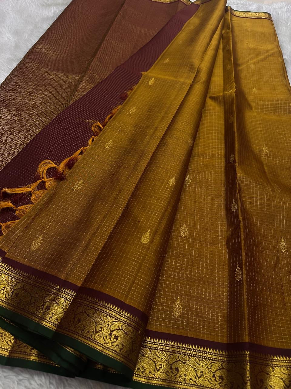 Amber Oosikattam ✨ – Pure Kanchipuram Silk Saree
Burnished Amber-Gold Body in Oosi Zari Kattam with Leaf Buttas
Deep Maroon Korvai Border with Green Selvedge & Elephant Motifs
Regal Maroon Pallu with Intricate Gold Zari Brocade
Silk Mark Certified |