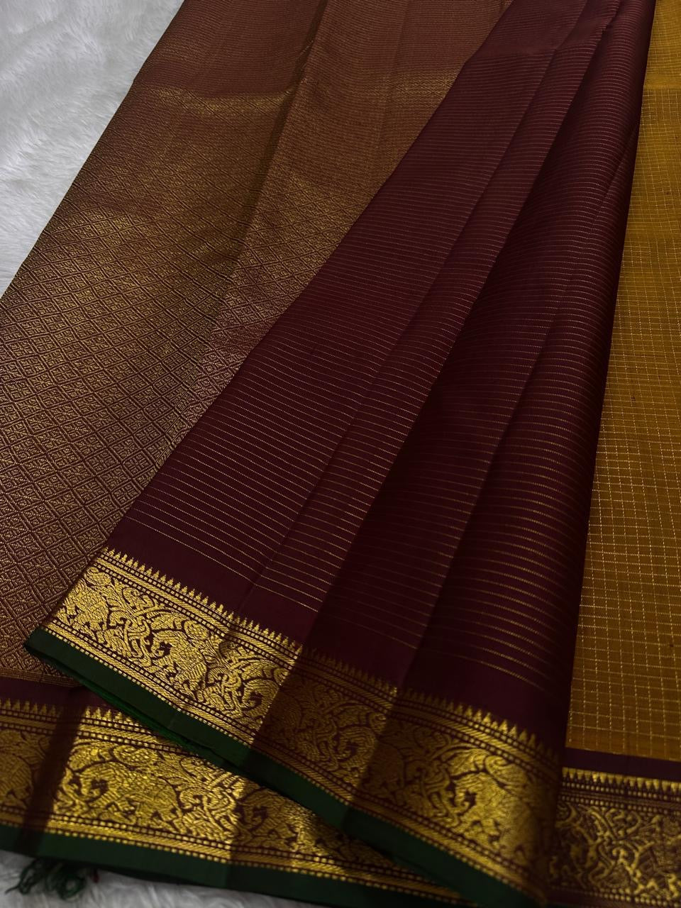 Amber Oosikattam ✨ – Pure Kanchipuram Silk Saree
Burnished Amber-Gold Body in Oosi Zari Kattam with Leaf Buttas
Deep Maroon Korvai Border with Green Selvedge & Elephant Motifs
Regal Maroon Pallu with Intricate Gold Zari Brocade
Silk Mark Certified |