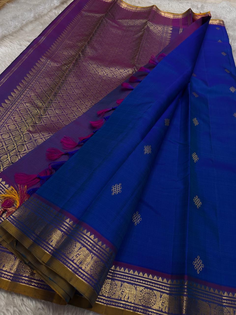 Sapphire Orchid celebrates the classic blue–purple pairing of Kanchi. The body is a rich sapphire/cobalt blue with tiny floral buttas in gold zari. A striking amethyst-purple korvai border and grid pavun Zari pallu Silk Mark Certified, delivery in 2 weeks
