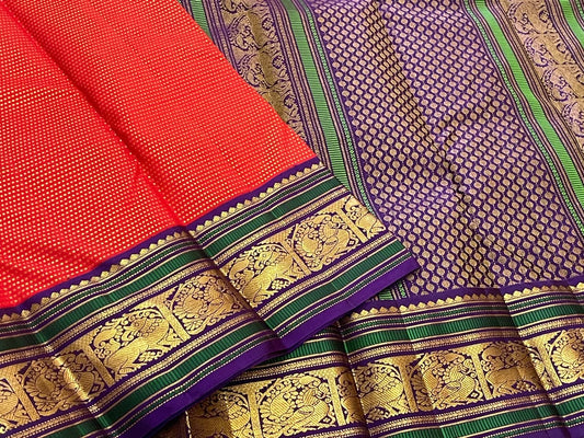 Handwoven Kancheepuram Butta saree in deep red with all-over dense gold zari butta and deep purple green Mayil Yazhi Butta border, full folded view