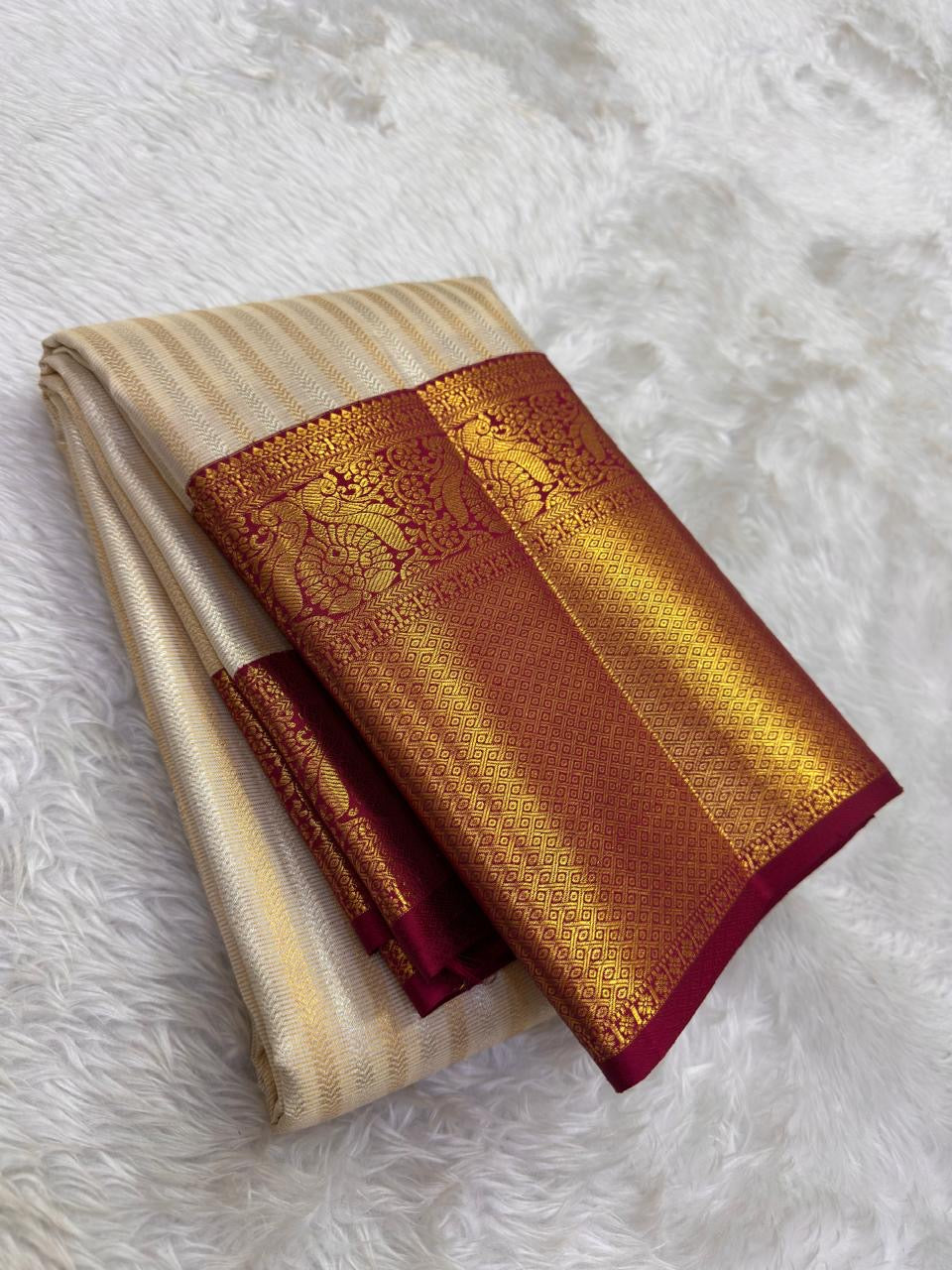 Full folded view of Kanchi Pattu Butta saree showing ivory ornate zari body and crimson peacock border contrast
