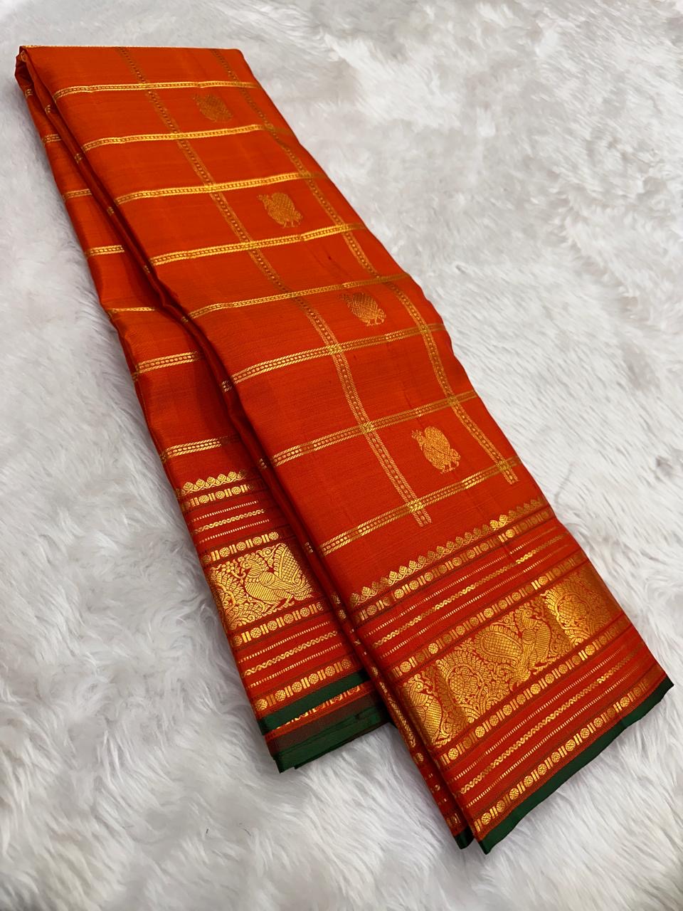 Handwoven Kanchipuram Zari Kattam saree in burnt orange with green selvedge, Kamalam Butta, and Mayil Butta gold zari border, full folded view