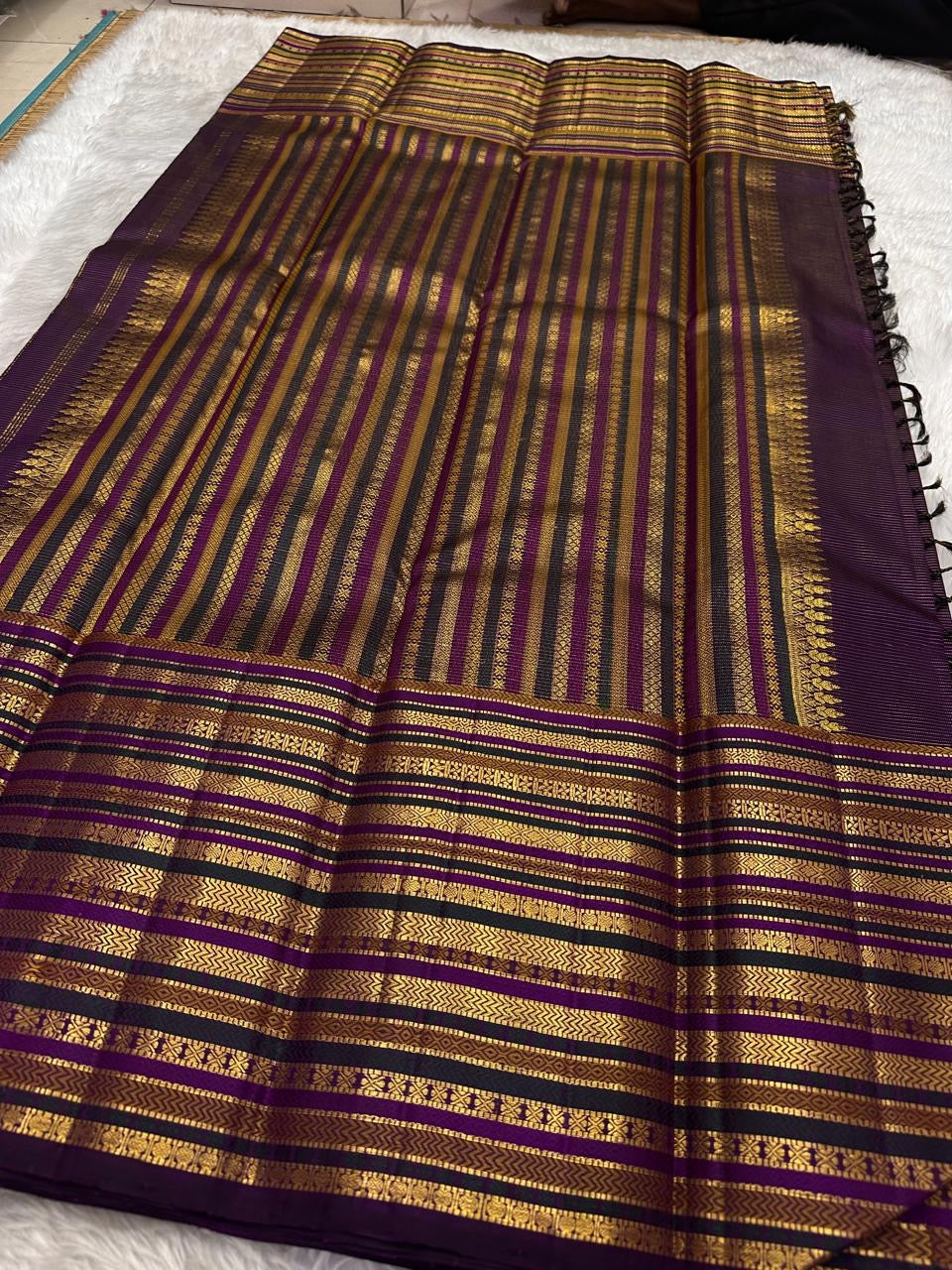 Folded view of the handwoven deep purple Kanjeevaram pure silk saree showing full body Varisaipet in gold zari from body to pallu