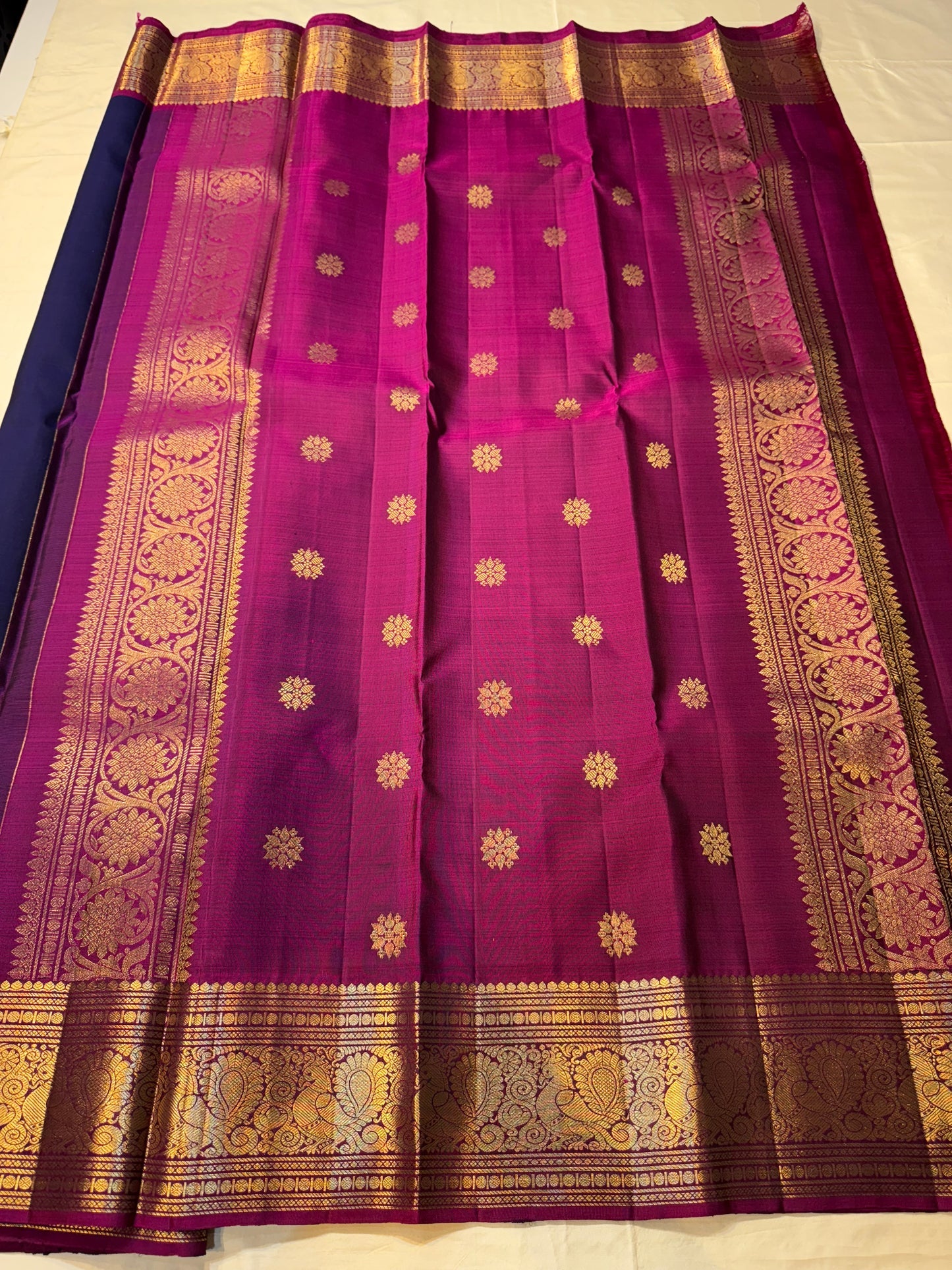 Angled view of navy body with gold elephant buttas, contrast magenta edge, and detailed zari woven border on a Pure Kanchipuram silk saree.