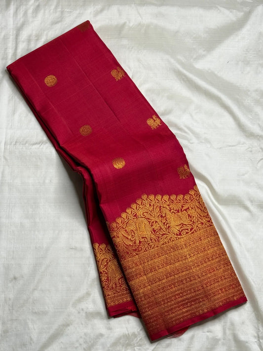 Folded Red Deep Pink Kanchipuram Butta saree showing antique-gold figurative Turning Border and fine zari registers.