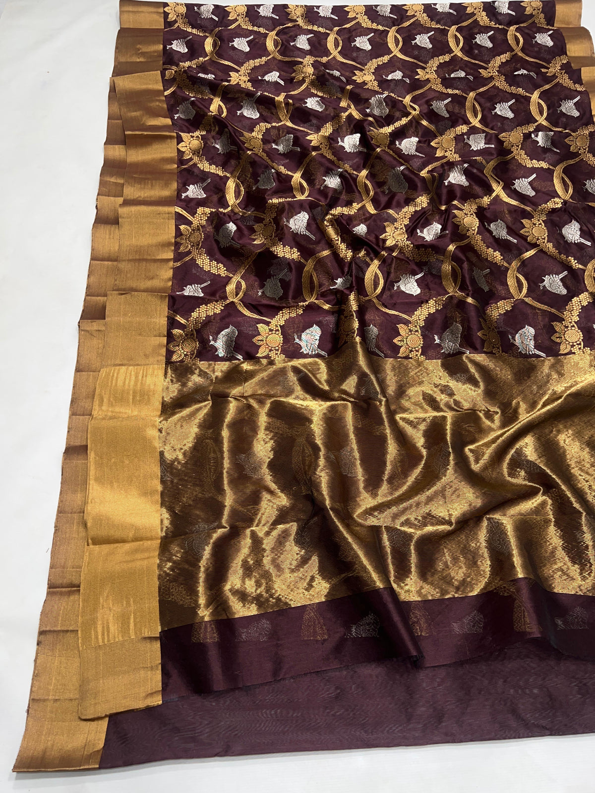 Folded Deep Cocoa Brown Pattu Silk Chanderi showing contrasting gold floral vines and silver-tone bird motifs.