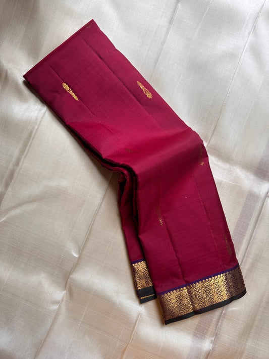 Draped maroon Pure Kanchipuram silk saree showing scattered zari buttas and a gold zari woven border with a dark edge finish.