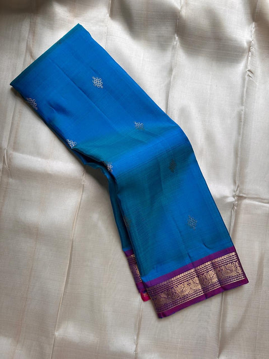 Draped teal blue Pure Kanchipuram silk saree showing scattered zari buttas and a purple border with zari woven pattern work.