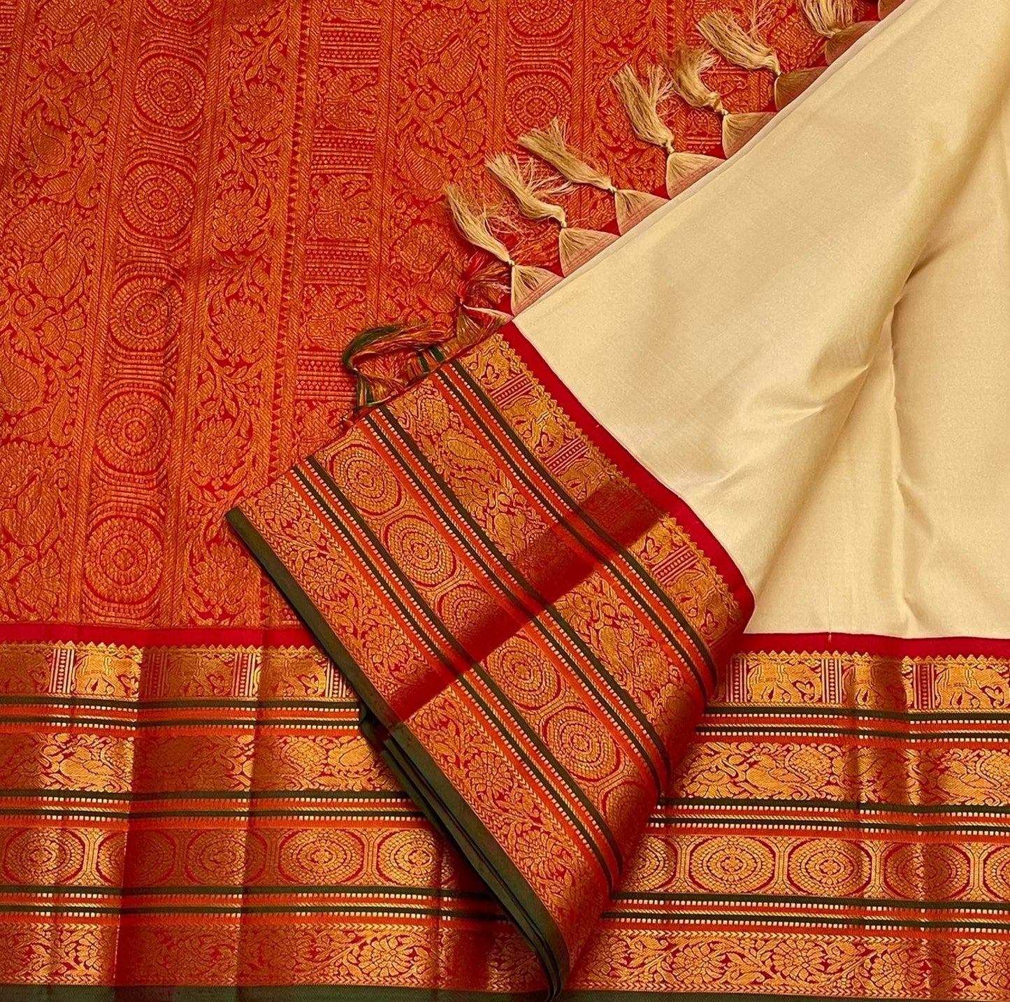 Flat-lay of red zari woven border with circular motifs and green edge on an ivory pure Kanchipuram silk saree.