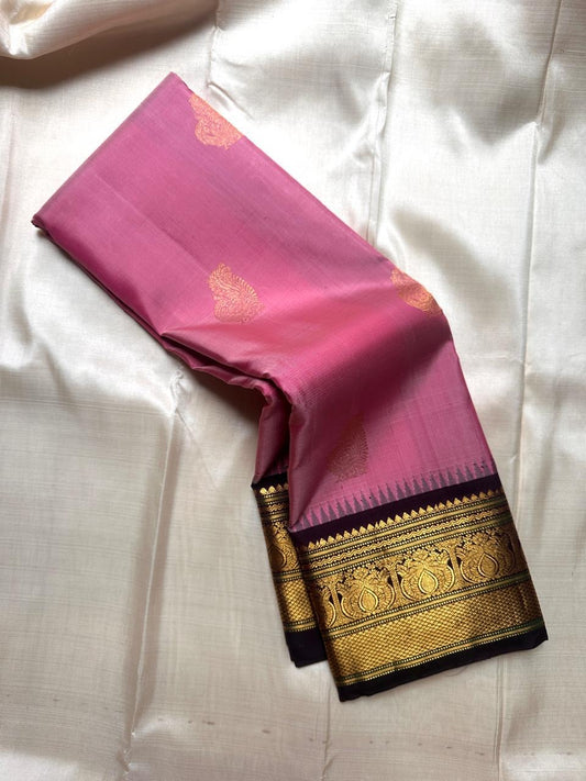 Pink Pure Kanchipuram Silk Saree with scattered gold buttas and black zari woven border shown on light fabric background