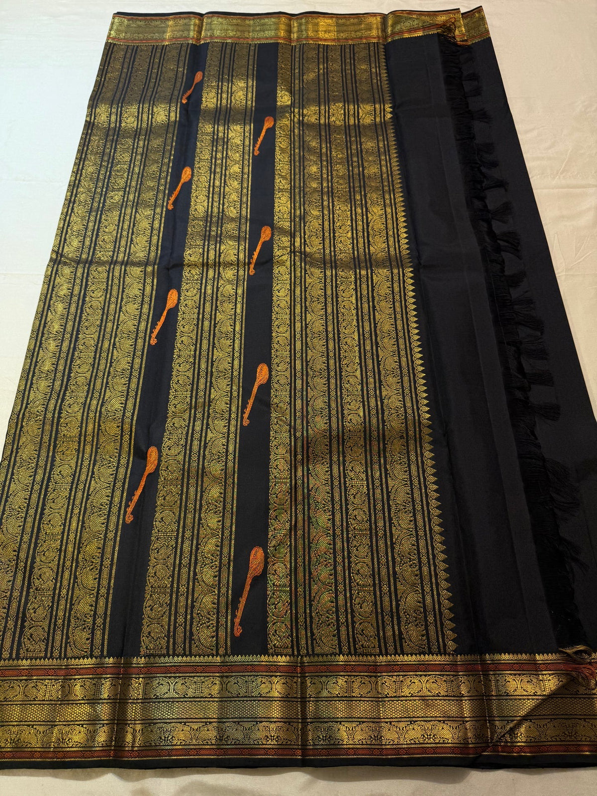 Self-colour black border with layered gold-zari bands and ornamental floral / paisley-like detailing.