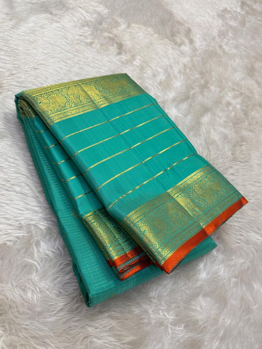 Narrow flame-orange selvedge along the elaborate gold zari border of mayil kazhuthu-inspired teal silk.