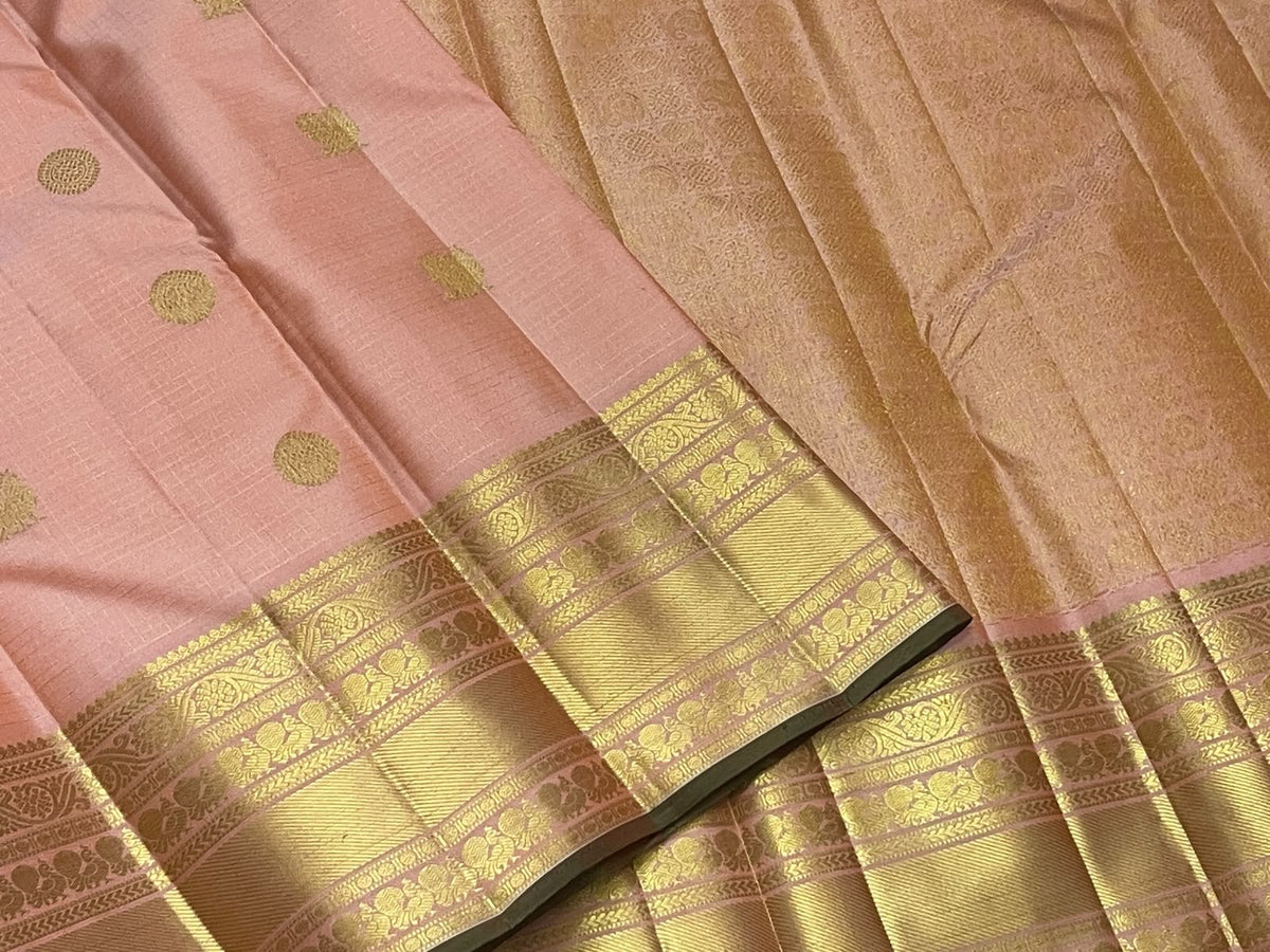 Soft peach-pink Kanchipuram body showing a fine classic-gold Zari Kattam grid beneath spaced zari buttas.