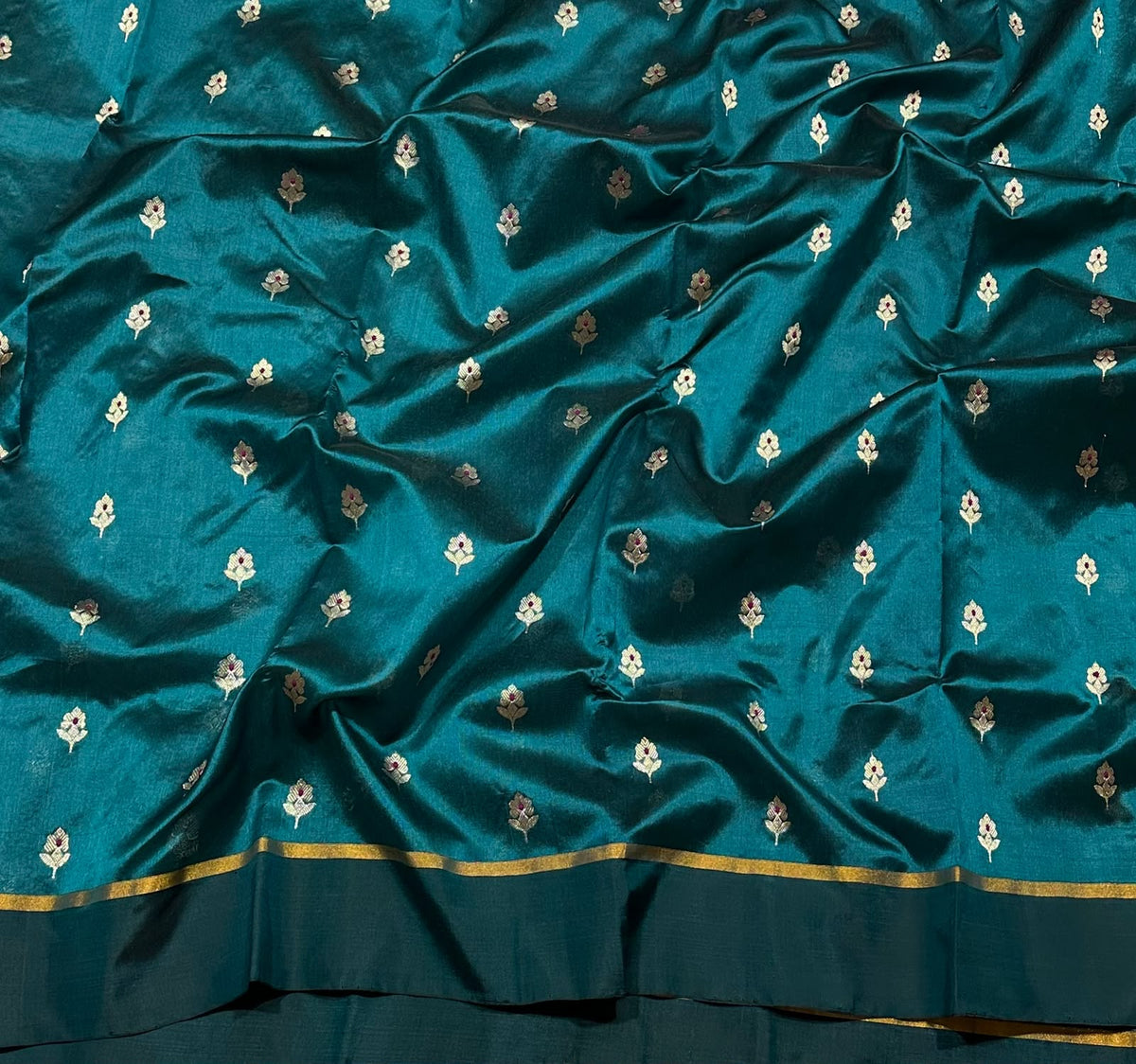 Delicate floral buttas woven across the peacock teal body of a Chanderi saree.