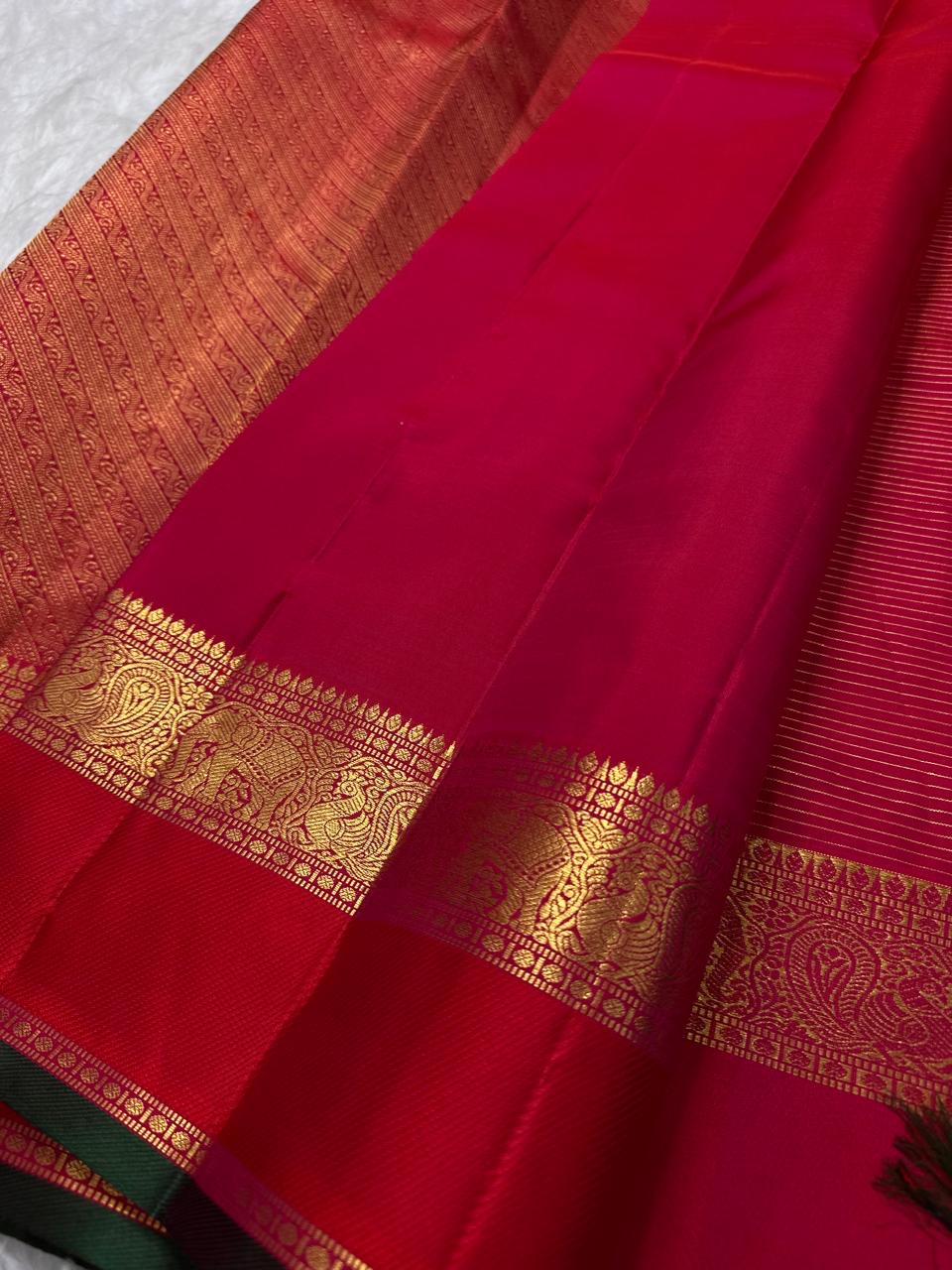 Close-up of raspberry pink and vermilion Pure Silk Kanchipuram saree with gold zari elephant and peacock border motifs.