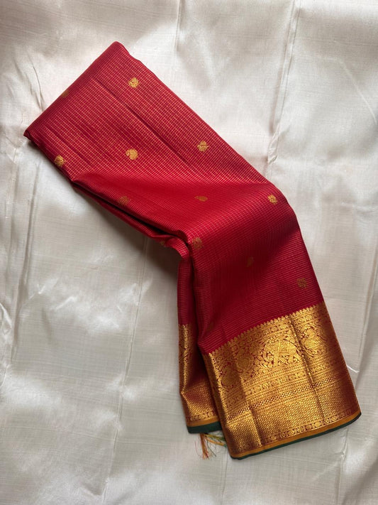 Folded deep red Kanchipuram silk saree highlighting antique gold zari border detail